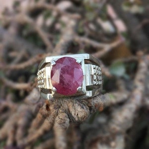 Peut inclure: Une bague en argent avec une grande pierre précieuse rose de forme ovale sertie au centre. La bague a une bande texturée.