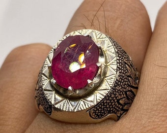 May include: A silver ring with a large, oval-shaped, red gemstone set in a detailed, ornate setting.