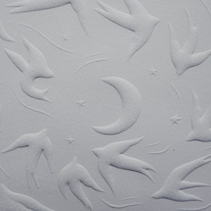 May include: A textured, off-white surface featuring an embossed pattern of swallows, stars, and a crescent moon. The design has a subtle, three-dimensional effect, creating a celestial theme.