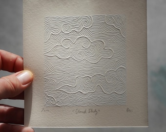 May include: A square, off-white print featuring a textured cloud design. The artwork, titled "Cloud Study," displays a series of swirling and wavy lines, creating a three-dimensional effect. The print is held by a hand.