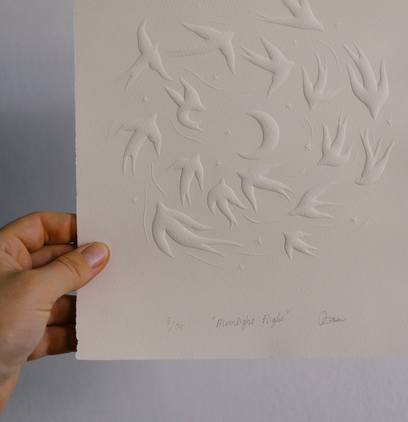 May include: A cream-colored print featuring embossed swallows in flight, a crescent moon, and stars. The artwork is titled "Moonlight Flight" and is numbered 5/75. The artist's signature is visible.