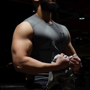 Può includere: Un uomo con una canotta grigia che flette il braccio, con la scritta "Maximum Muscle Gain". L'immagine promuove un programma di 8 settimane per muscoli, cardio e forza di Shorif Rahman. Sono visibili anche le parole "Hybrid Training".