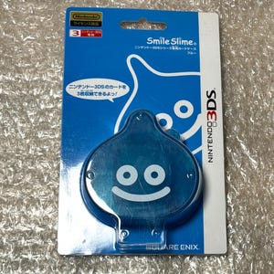 May include: A blue Smile Slime Nintendo 3DS card case. The case is shaped like a blue slime character with a smiling face. The packaging is blue and white with Japanese text and the Nintendo 3DS logo.