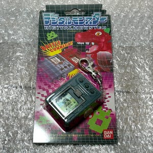 May include: A gray Digital Monster keychain with a blue screen and the text "BATTLE CONNECT!" on the packaging. The packaging also features a red dinosaur character.