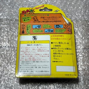 K&ouml;nnte beinhalten: Gelbe und wei&szlig;e Verpackung f&uuml;r ein Spielzeug mit einer Dinosaurier-Illustration. Die Verpackung enth&auml;lt Anweisungen in Japanisch, darunter der Text "ボタン電池LR-44 2個使用" und "対象年齢12才以上".