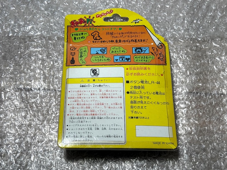 K&ouml;nnte beinhalten: Gelbe und wei&szlig;e Verpackung f&uuml;r ein Spielzeug mit einer Dinosaurier-Illustration. Die Verpackung enth&auml;lt Anweisungen in Japanisch, darunter der Text "ボタン電池LR-44 2個使用" und "対象年齢12才以上".