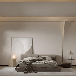 Op de afbeelding: Een minimalistische slaapkamer met een groot bed, een nachtkastje en een ingelijst kunstwerk aan de muur. De kamer is geschilderd in een licht beige kleur en heeft een houten vloer.