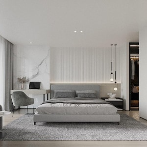 Op de afbeelding: Een moderne slaapkamer met een grijs gestoffeerd bed, wit beddengoed en een grijze fauteuil. De kamer heeft een wit plafond, witte muren en een groot raam met transparante gordijnen. Er is een witte marmeren muur achter het bed en een zwart-wit abstract schilderij aan de muur rechts.