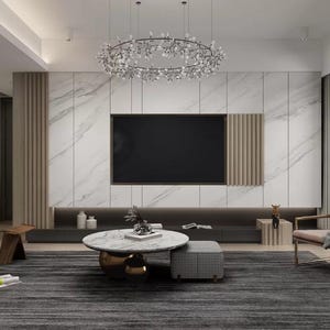 Puede incluir: Un salón moderno con una gran pantalla de televisión negra montada en una pared de mármol blanco. La sala cuenta con una mesa de centro redonda grande con una base dorada y una alfombra gris. Hay dos sillones de cuero marrón, uno con una manta, y una mesa auxiliar de madera con un jarrón de flores.