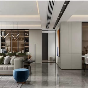 Puede incluir: Un salón moderno con un gran sofá blanco, una mesa de café y un otomano azul. La habitación tiene grandes ventanas con cortinas grises, una estantería y una mesa de comedor con sillas.