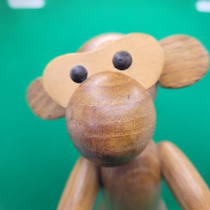 May include: A wooden monkey figurine with a brown body and a large, round nose. The monkey has black eyes and a brown wooden face.