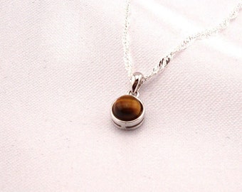 Può includere: Una collana con catena d'argento con un piccolo ciondolo rotondo con una pietra di occhio di tigre marrone.