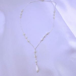 Pu&ograve; includere: Una delicata collana a catena color argento con un design a goccia a forma di Y. La collana &egrave; impreziosita da piccole perline rotonde color bianco sporco distanziate lungo la catena, che terminano con una singola perla bianca allungata a goccia.