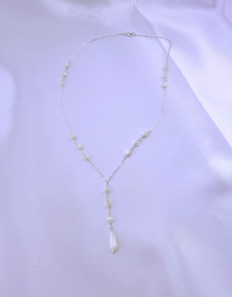 Pu&ograve; includere: Una delicata collana a catena color argento con un design a goccia a forma di Y. La collana &egrave; impreziosita da piccole perline rotonde color bianco sporco distanziate lungo la catena, che terminano con una singola perla bianca allungata a goccia.