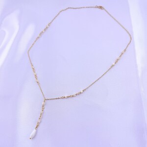 Pu&ograve; includere: Una collana a catena color oro con un design a goccia a forma di Y. La sottile catena in metallo &egrave; impreziosita da piccole perline bianche distanziate uniformemente e termina con una singola perla bianca allungata a forma di goccia.