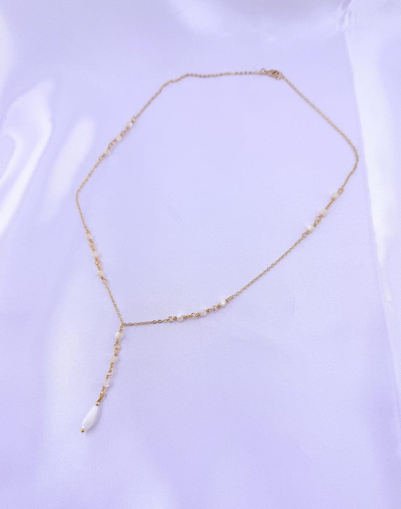 Pu&ograve; includere: Una collana a catena color oro con un design a goccia a forma di Y. La sottile catena in metallo &egrave; impreziosita da piccole perline bianche distanziate uniformemente e termina con una singola perla bianca allungata a forma di goccia.