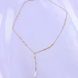 Pu&ograve; includere: Una collana a catena color oro con un design a goccia a forma di Y. La sottile catena in metallo &egrave; impreziosita da piccole perline bianche distanziate uniformemente lungo i lati, che portano a un filo verticale centrale terminante in una perla a goccia.