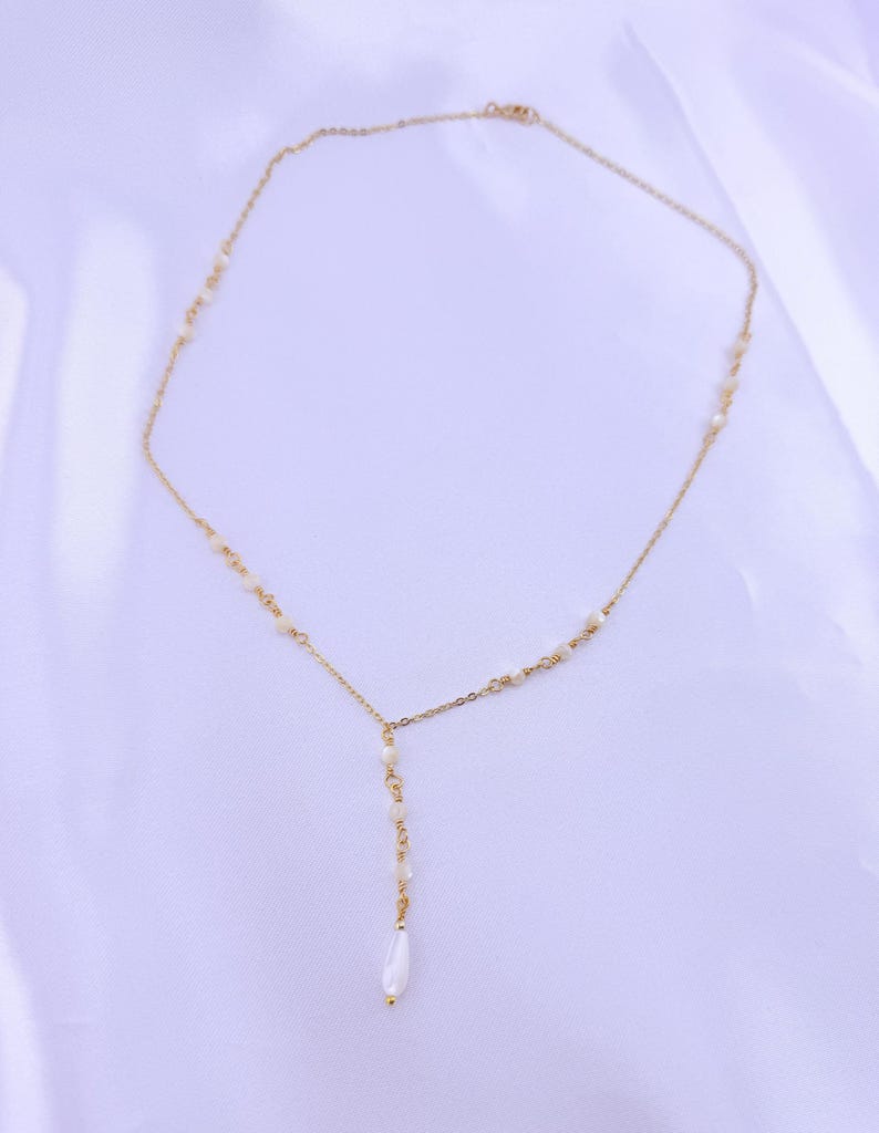 Pu&ograve; includere: Una collana a catena color oro con un design a goccia a forma di Y. La sottile catena in metallo &egrave; impreziosita da piccole perline bianche distanziate uniformemente lungo i lati, che portano a un filo verticale centrale terminante in una perla a goccia.
