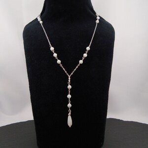 Pu&ograve; includere: Una collana a Y caratterizzata da una sottile catenina color argento decorata con piccole perle rotonde color bianco sporco distribuite uniformemente. La collana termina con una singola perla allungata a goccia nel punto centrale.
