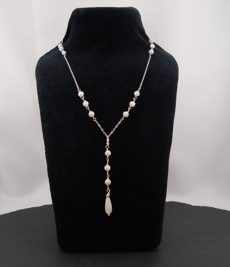 Pu&ograve; includere: Una collana a Y caratterizzata da una sottile catenina color argento decorata con piccole perle rotonde color bianco sporco distribuite uniformemente. La collana termina con una singola perla allungata a goccia nel punto centrale.