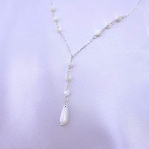 Pu&ograve; includere: Una delicata collana a catena color argento con un design a goccia a forma di Y. La catena &egrave; impreziosita da piccole perline bianche iridescenti rotonde distanziate lungo le maglie, che terminano con una singola perla bianca liscia a goccia.