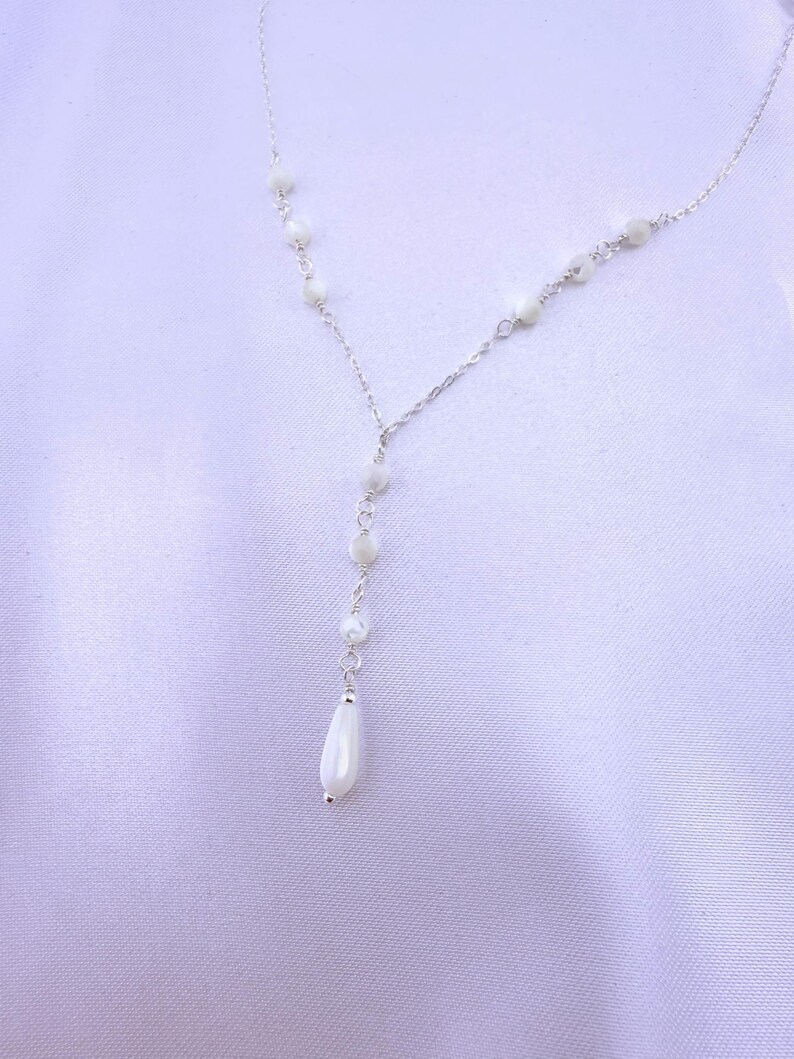 Pu&ograve; includere: Una delicata collana a catena color argento con un design a goccia a forma di Y. La catena &egrave; impreziosita da piccole perline bianche iridescenti rotonde distanziate lungo le maglie, che terminano con una singola perla bianca liscia a goccia.