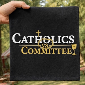 Op de afbeelding: Zwart rechthoekig textiel met de tekst "Catholics vs Committee" in wit en goud. Het ontwerp bevat een gouden kruis, een doornenkroon en een kelk.
