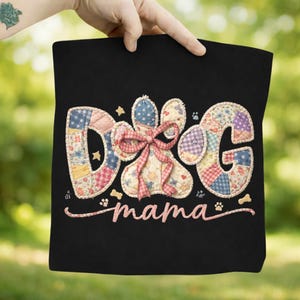 May include: Black tote bag featuring the word "DOG" in patchwork letters and a paw print design. The word "mama" is written in cursive below the paw print. The letters and paw print are decorated with a pink bow.