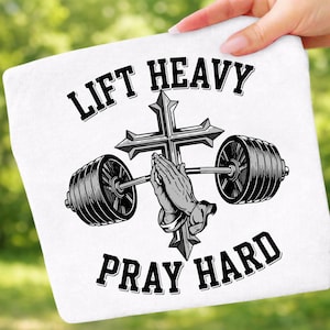 May include: White towel with the text "LIFT HEAVY PRAY HARD" in black. The design features a barbell with weights on each end, a cross, and praying hands. The towel is held up by a hand.