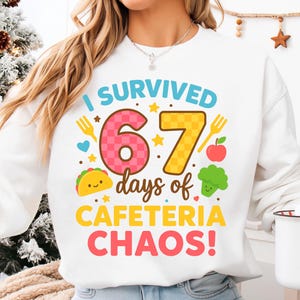 Könnte beinhalten: Weißes Sweatshirt mit dem farbenfrohen Text "I SURVIVED 67 days of CAFETERIA CHAOS!". Das Design umfasst eine rosa 6, eine gelbe 7 und Essenssymbole wie einen Taco, einen Apfel und Brokkoli.