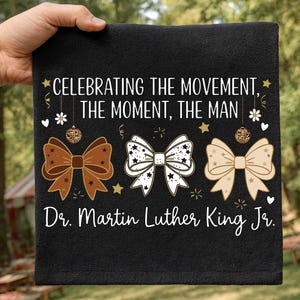 May include: Black towel with the text "CELEBRATING THE MOVEMENT, THE MOMENT, THE MAN" and "Dr. Martin Luther King Jr." in white. The design includes three bow ties in brown, white, and beige.