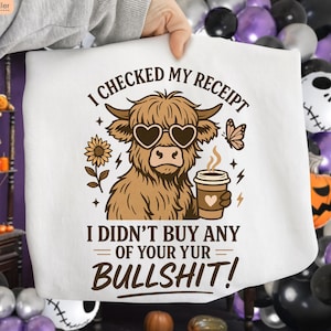 May include: White graphic tee featuring a cartoon Highland cow wearing heart-shaped sunglasses and holding a coffee cup. The text reads "I CHECKED MY RECEIPT, I DIDN'T BUY ANY OF YOUR YUR BULLSHIT!" with sunflower and butterfly accents.
