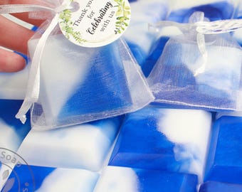 May include: Blue and white soap bars with a marbled design, some packaged in sheer white bags with a tag that reads "Thank you for Celebrating with us". The soaps are arranged in a grid pattern.