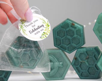 May include: Hexagon-shaped teal soaps with a honeycomb pattern, some in a sheer bag with a tag that reads "Thank you for Celebrating with us." The soaps are arranged on a white surface.