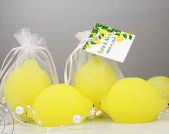 May include: Five yellow lemon-shaped soaps wrapped in white tulle bags with a white satin ribbon. The soaps are decorated with white pearl beads. A small white tag with the text "Sara & Alex March 17, 2023" is attached to one of the bags.