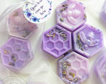 May include: Hexagonal purple soap bars featuring embossed bee and honeycomb patterns, embedded with dried lavender buds. Each soap is individually wrapped in a white organza drawstring bag with a circular tag that reads, Your text can go here.