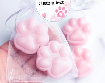 May include: Three light pink, paw-shaped soaps. Two soaps are inside a sheer white organza drawstring bag, and one is outside. A round white tag attached to the bag features pink paw prints, a small heart, and the text Custom text.