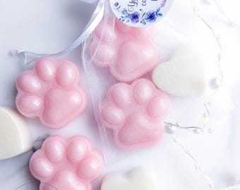 May include: Pink paw-shaped soaps and white heart-shaped soaps, with some inside a white organza drawstring bag. A circular tag attached to the bag features a floral border and the text "Your text can go here" in a dark blue script font.