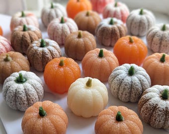 May include: A collection of small, decorative pumpkin-shaped items in various colors including orange, white, beige, and brown. Each pumpkin features a textured surface with vertical ridges and a small, distinct green stem at the top center.