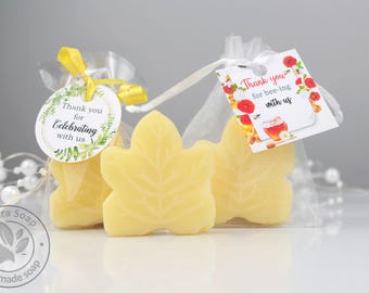 May include: Two pale yellow leaf-shaped soaps packaged in sheer white organza bags. One bag has a round tag reading Thank you for Celebrating with us with green leaves. The other has a square tag reading Thank you for bee-ing with us with flowers.