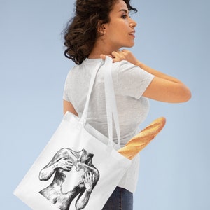 Può includere: Una borsa tote bianca con un'illustrazione in bianco e nero di una persona che tiene il suo cuore. La persona è raffigurata con le mani che le coprono il petto. La borsa è portata da una persona che indossa una maglietta grigia e jeans blu. Un baguette è infilato nella borsa.