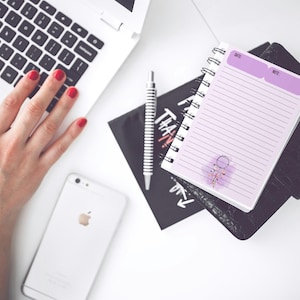 May include: A purple and white lined notebook with a spiral binding. The notebook has a pink and white floral design with a dreamcatcher in the center. The notebook has the words "Date" and "Note" at the top.