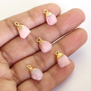 May include: Five pink gemstone charms with gold-plated settings. The charms are shaped like irregular, faceted stones and have a loop at the top for attaching to jewellery.
