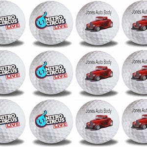 May include: Twelve white golf balls with different designs. Six balls feature a blue and red logo that says "Nitro Circus Live". Six balls feature a red hot rod car with the text "Jones Auto Body".