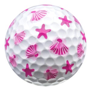 May include: White golf ball decorated with pink starfish and seashell designs. The golf ball has a dimpled surface and is designed for recreational use. The pink accents provide a decorative touch to the golf ball.