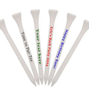 K&ouml;nnte beinhalten: F&uuml;nf wei&szlig;e Golf-Tees mit personalisierten Botschaften. Die Botschaften lauten "Happy Birthday Sam!" in Blau, "Eric's Bach Party 2024" in Rot, "Your text here" in Gr&uuml;n und "Time to Par-Tee" in Gr&uuml;n.
