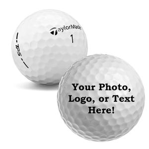 May include: Two white golf balls, one with the TaylorMade logo and the number 1, and the other with the text "Your Photo, Logo, or Text Here!"