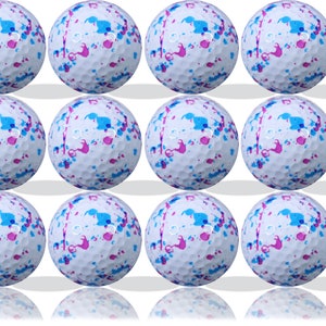 Puede incluir: Doce bolas de golf blancas con salpicaduras de pintura azul y rosa.