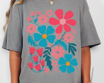 Puede incluir: Camiseta gris con un diseño floral colorido. El gráfico presenta flores rosas y turquesas con hojas verdes. La camiseta tiene un corte holgado y mangas cortas. El texto "creekstone clothing" está en la esquina inferior derecha.