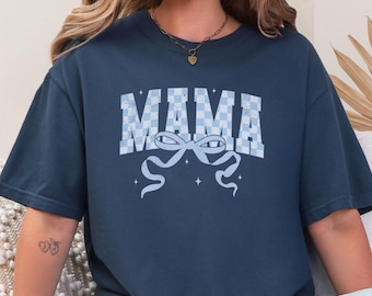Op de afbeelding: Marineblauw T-shirt met het woord "MAMA" in een lichtblauw geblokt patroon. Daaronder een lichtblauw strikdesign met linten. Het shirt heeft een relaxte pasvorm.